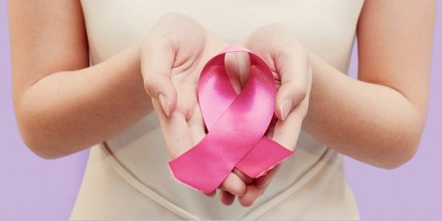 A person holds a large pink ribbon in both hands, symbolizing breast cancer awareness. The background is a soft purple, emphasizing the ribbon's vibrant color.